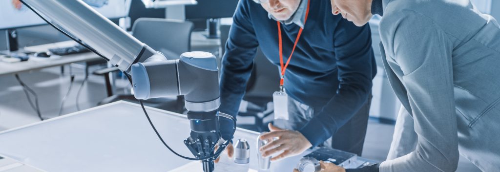 Two employees discuss work by a robotic arm.