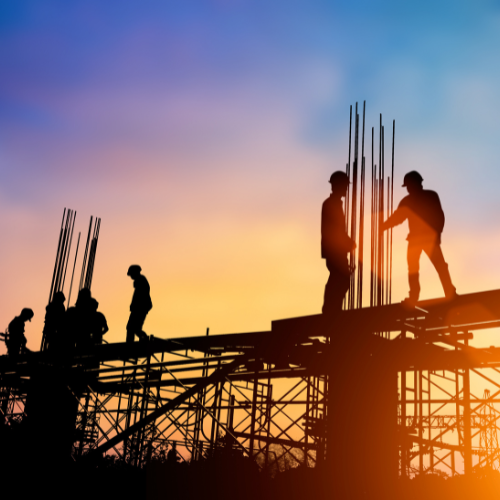 Construction workers stand on steelwork at sunset.